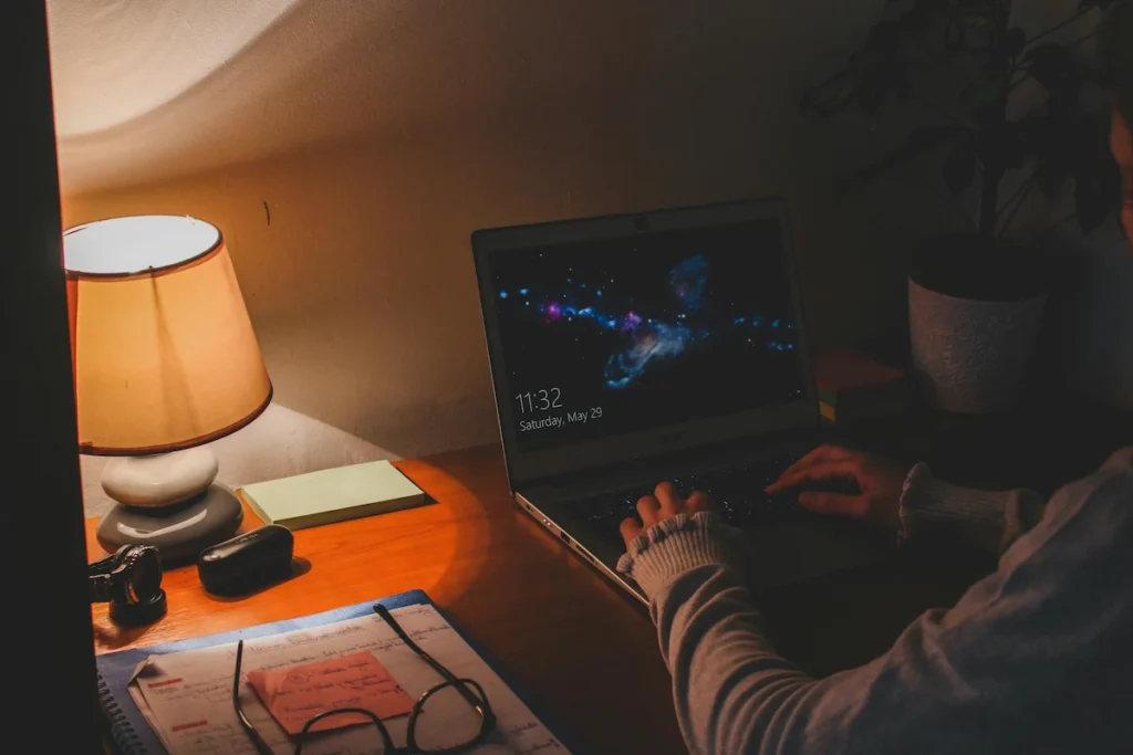 Person working late on a laptop with notebook and glasses at desk — symbolizing the real behind-the-scenes of running an online business in Trinidad.