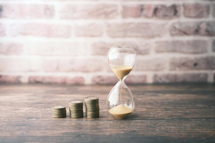 | Every Ingredient Stacked coins beside an hourglass representing the trade-off between money and time in business